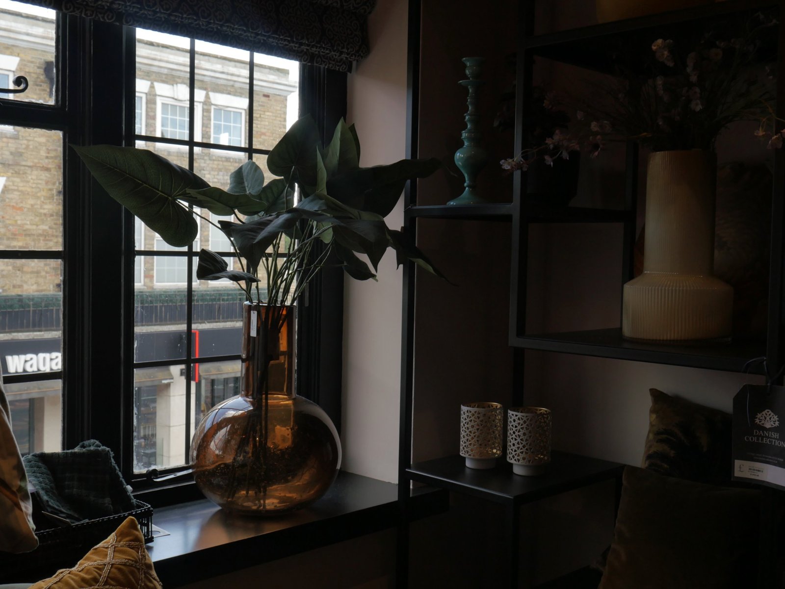 Amber glass vase of green leaves on a window sill beside black shelves