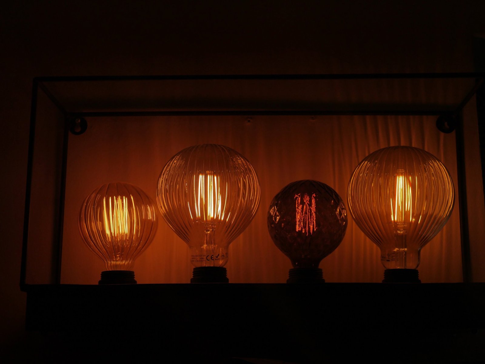 Four glowing filament bulbs in different glass shapes inside a metal frame