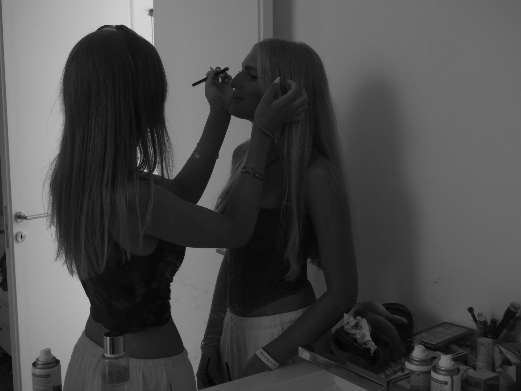 Black and white photograph of one girl applying eyeliner to another in a mirror