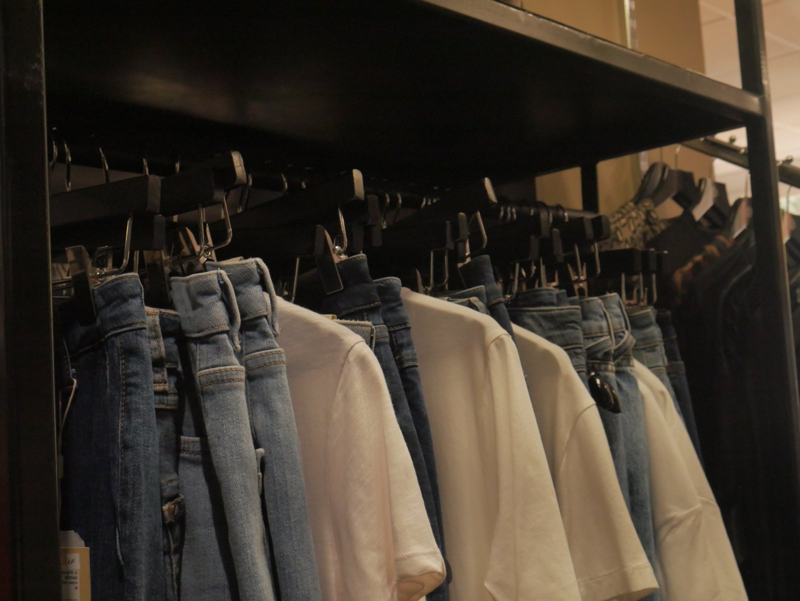 Denim and white T-shirts hanging on a dark store rail