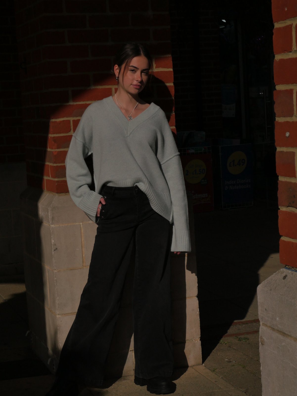 Full-length shot of the pale V-neck jumper with wide black trousers in dramatic shadow