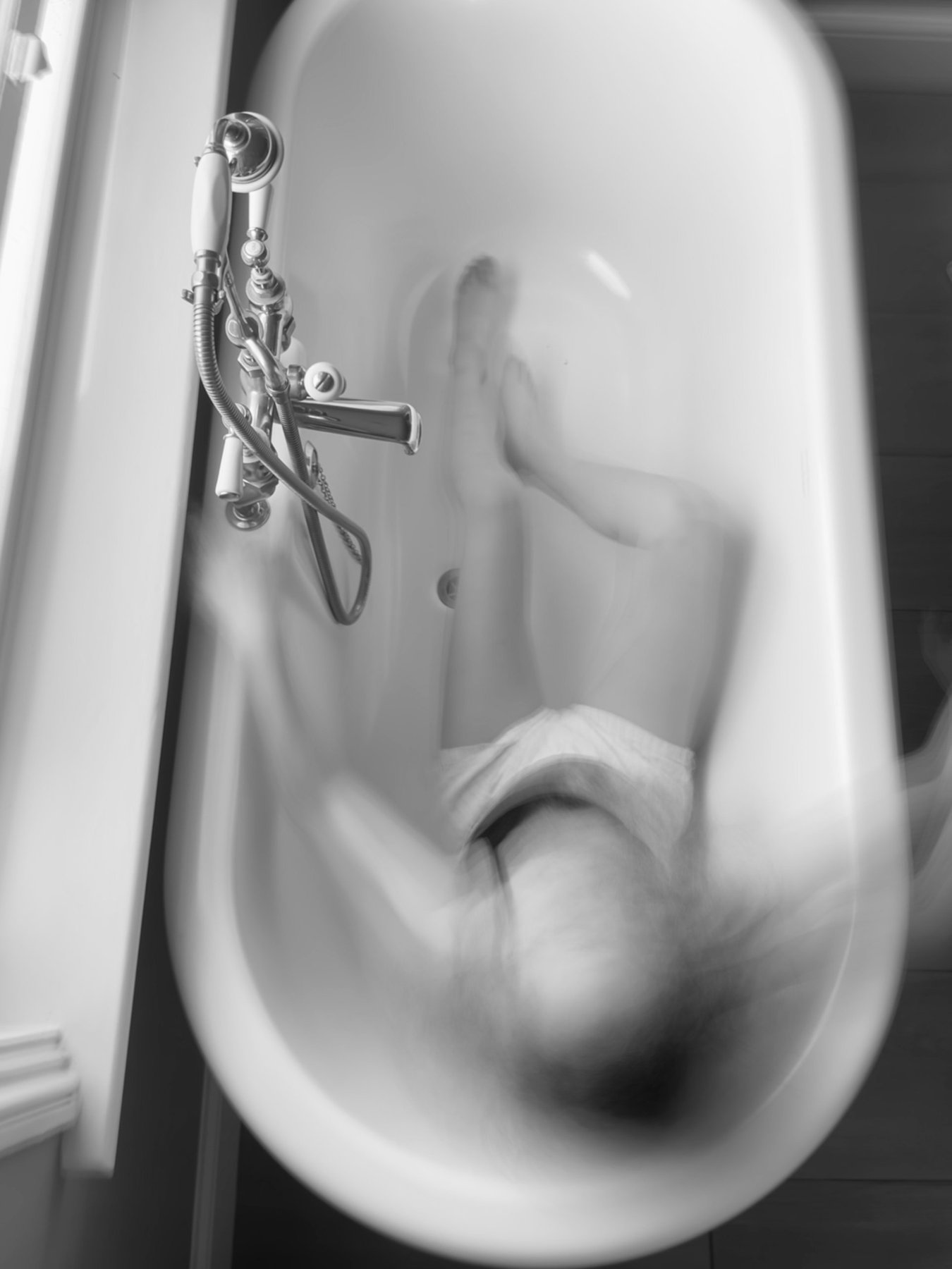 Black and white overhead shot of a blurred figure moving in a clawfoot bath