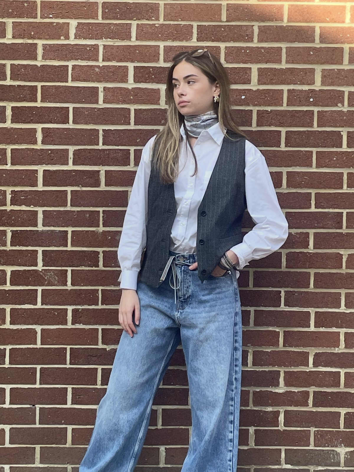 Model against a brick wall in a pinstripe waistcoat, silk scarf and wide-leg jeans