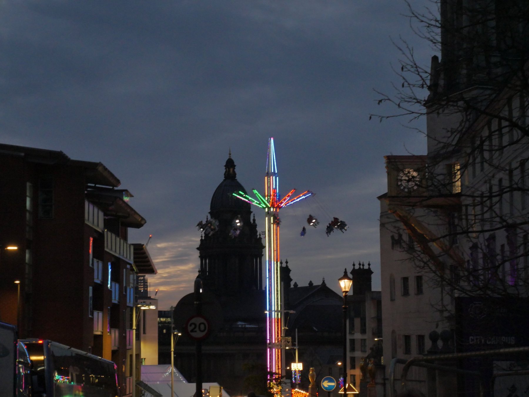 Neon-lit star flyer ride at dusk with the Leeds Town Hall dome behind