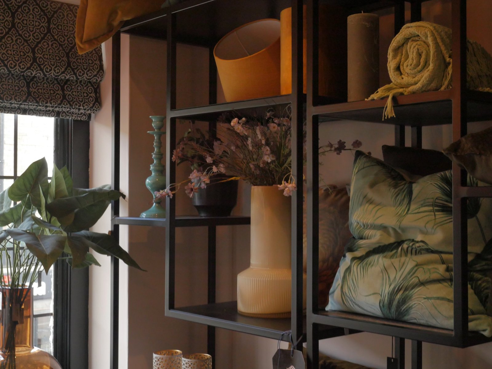 Black shelving styled with a mustard lampshade, candle, throw, vase and palm-print cushions
