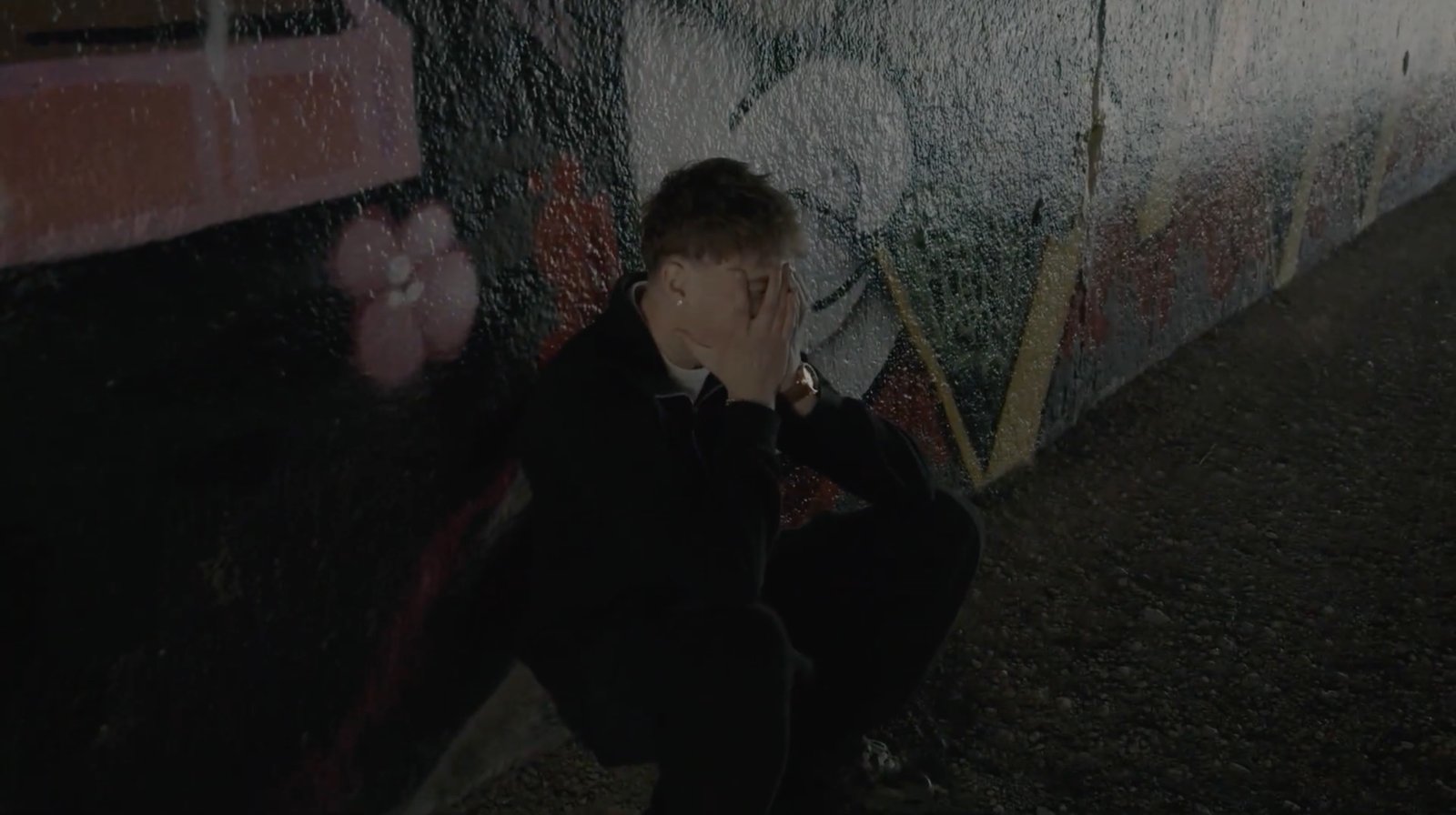 Cover: still from Out of Sight: Out of Mind, a young man crouched against a graffiti wall at night