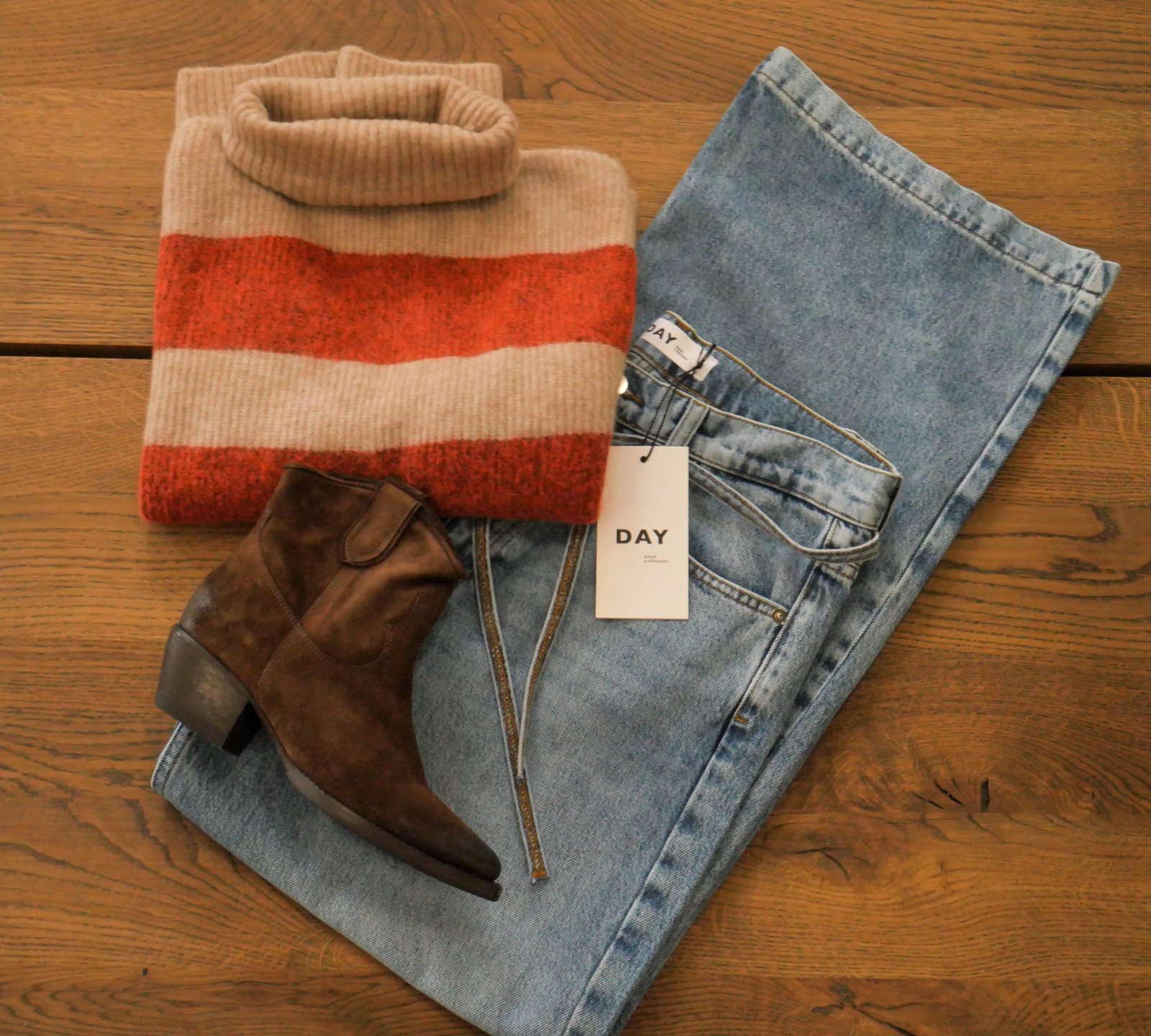 Flat lay of a striped knit, light-wash jeans and brown suede boots on a wooden table