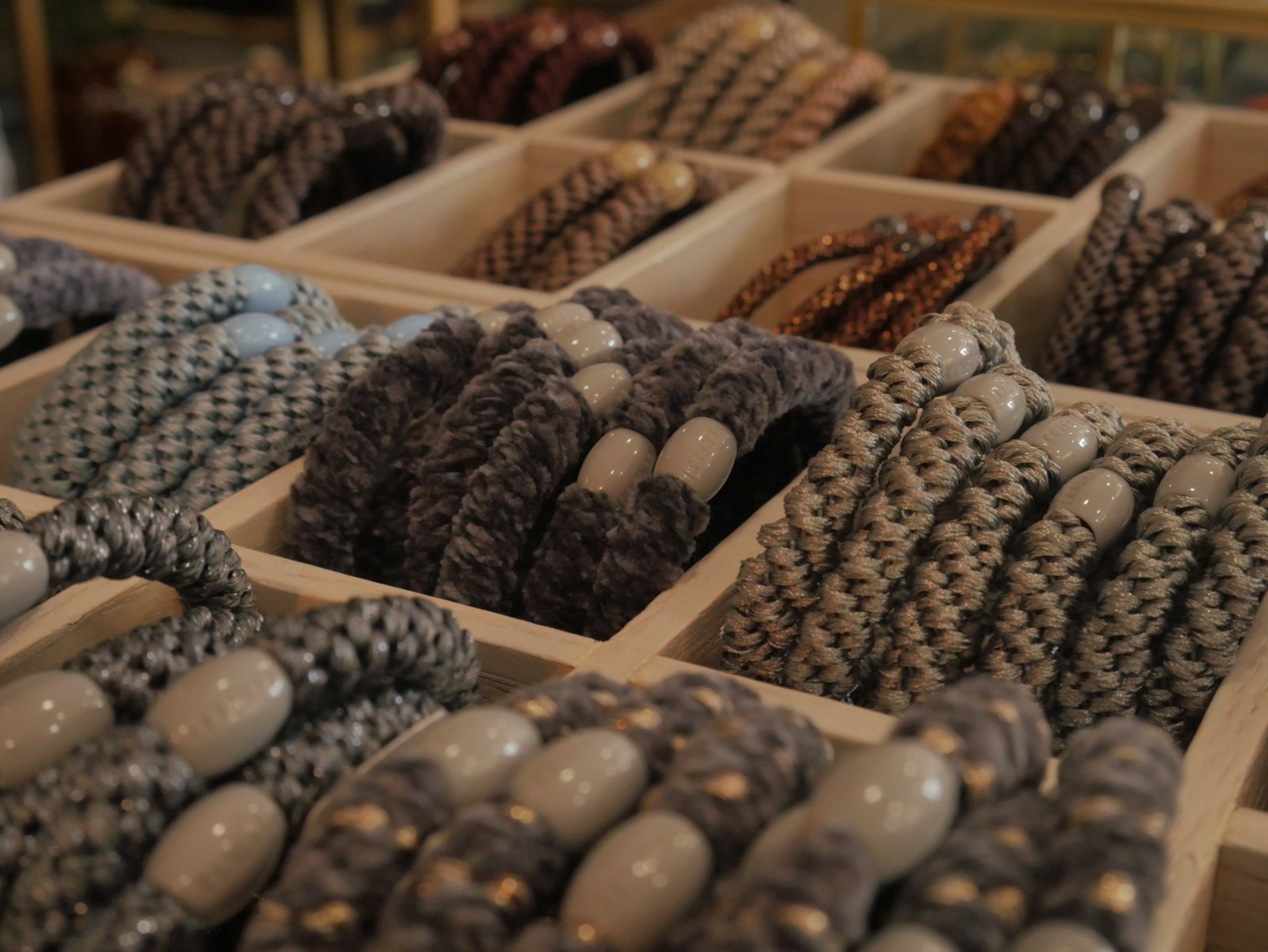 Wooden trays of woven hair ties in grey, blue and bronze