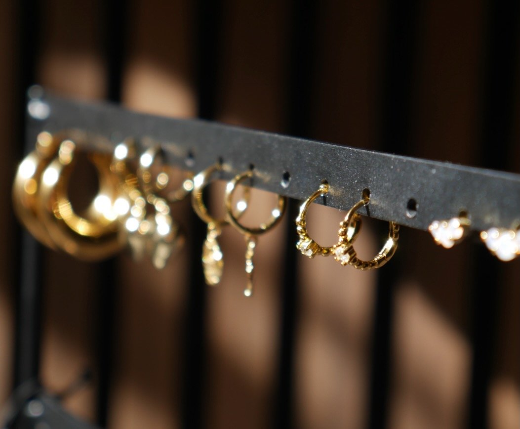 Gold hoop and stud earrings on a display bar in warm light