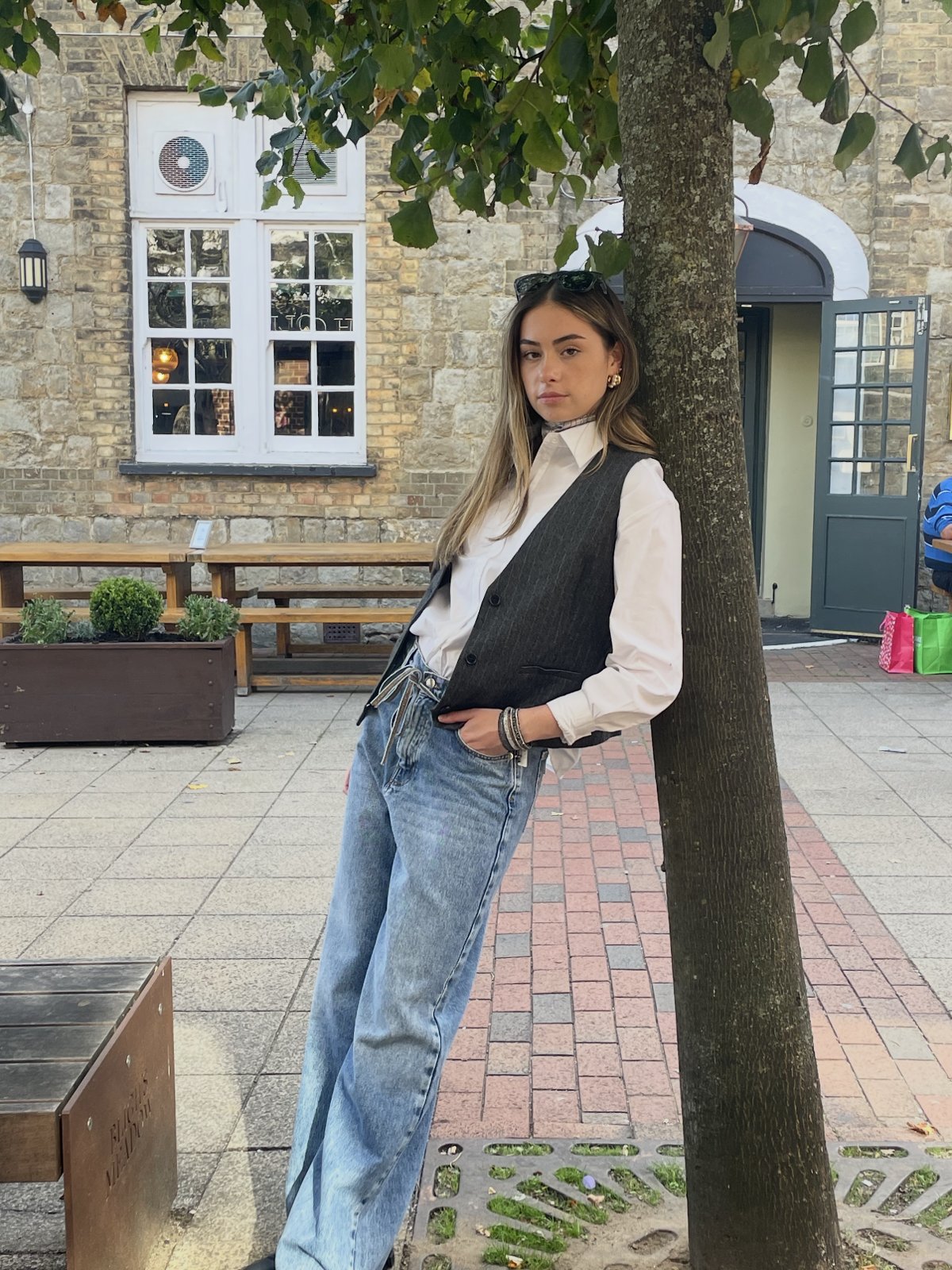Model leaning on a tree in a pinstripe waistcoat, white shirt and light-wash jeans